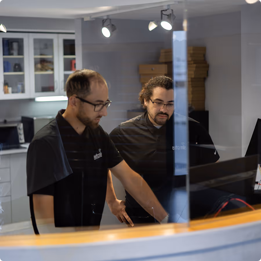 Two Extra Mile IT technicians looking a computer monitor, standing behind a curved window