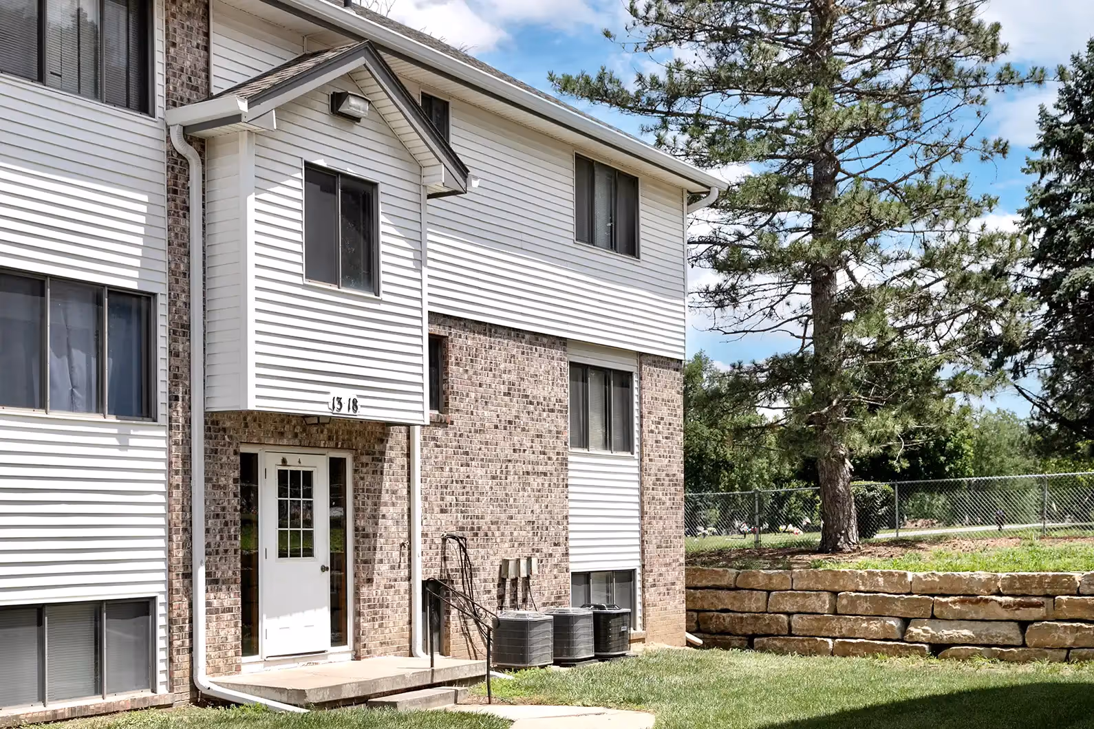 Multi-story residential building at Gold Coast featuring a combination of brick and white vinyl siding with manicured green space.