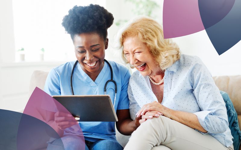A support worker and an elderly participant sitting on a couch, engaged with a tablet, sharing a moment of connection together.