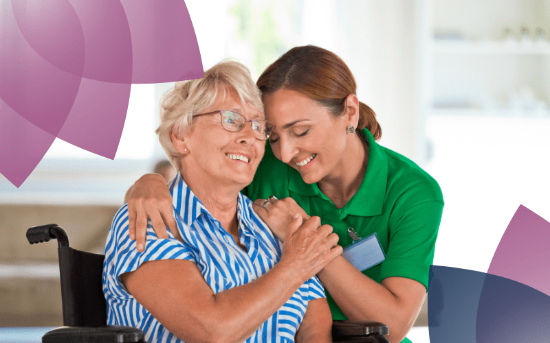 Age Care facility with a support worker supporting an elderly woman in a wheel chair.