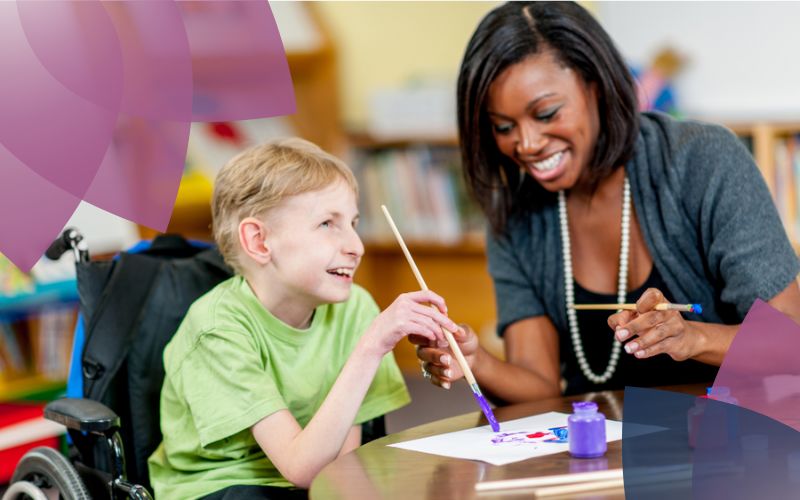 A participant in a wheelchair and his support worker joyfully create art together, fostering creativity and connection in a vibrant, inclusive environment.