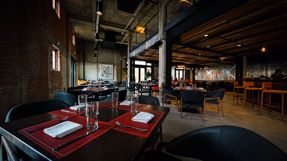 Industrial-style dining room at Love’s Barbecue & Oyster Bar inside Tannahill’s, featuring dark wood tables, red placemats, and neatly arranged glassware.