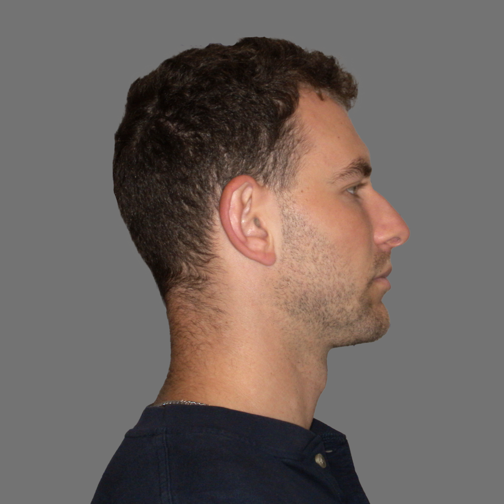 Profile of a young man with short hair and light stubble wearing a dark shirt against a gray background.