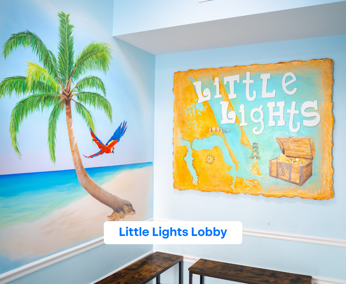 Lobby corner with mural of beach scene including a palm tree, a flying red and blue parrot, and a treasure map with 'Little Lights' text.