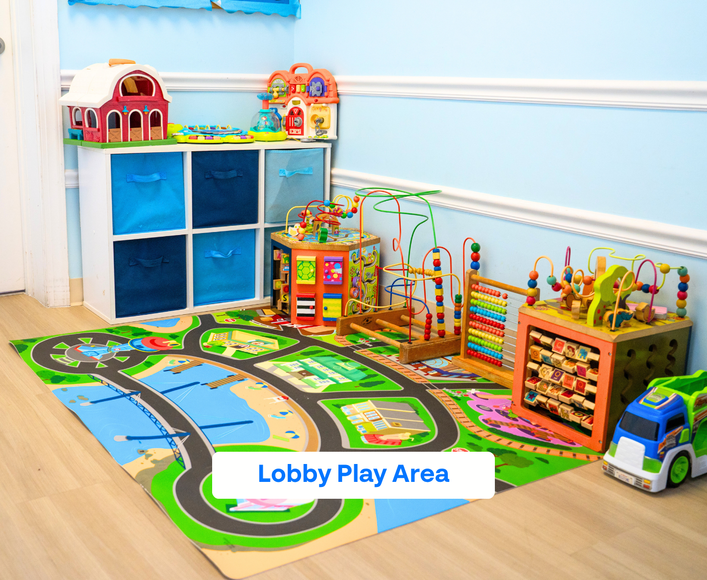 Colorful children's lobby play area with toy storage bins, activity cubes, and a play mat featuring roads and buildings.