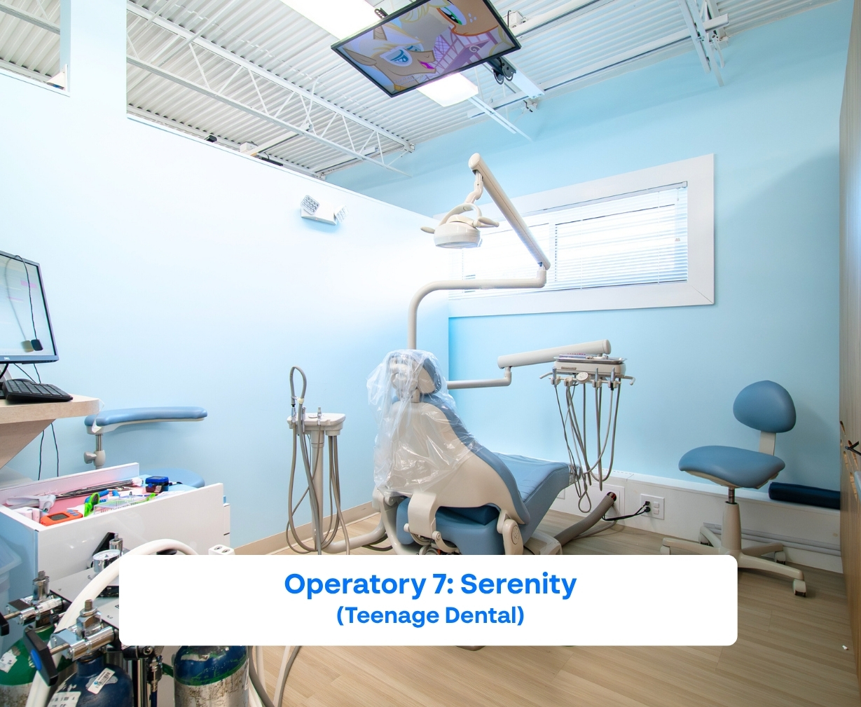 Bright pediatric dental operatory with light blue walls, dental chair, overhead light, and ceiling-mounted TV playing animation.