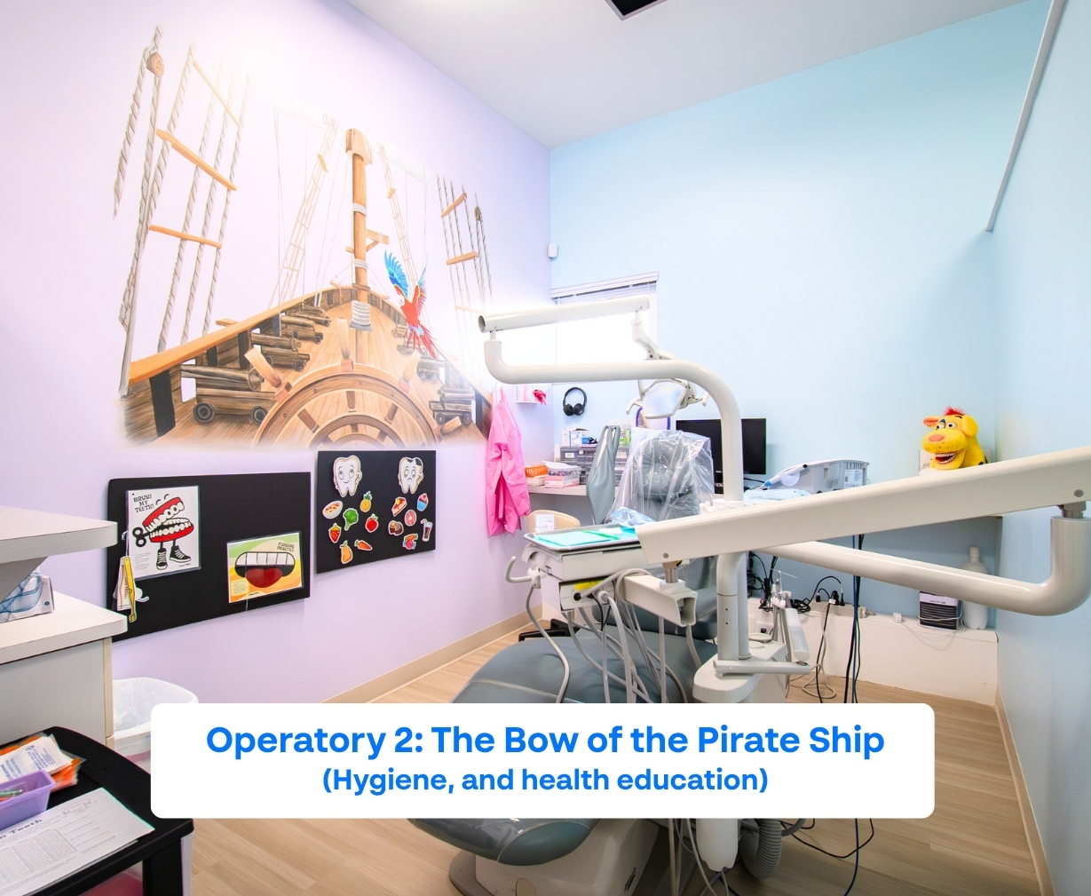Pediatric dental operatory with a mural of a pirate ship's bow, dental chair, educational posters about dental hygiene, and a stuffed toy on a table.