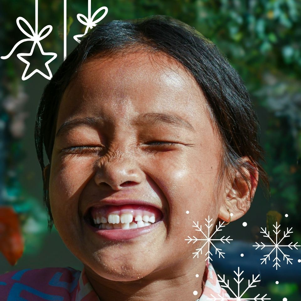 Close-up of a smiling child with eyes closed and missing front teeth, decorated with white star and snowflake illustrations.