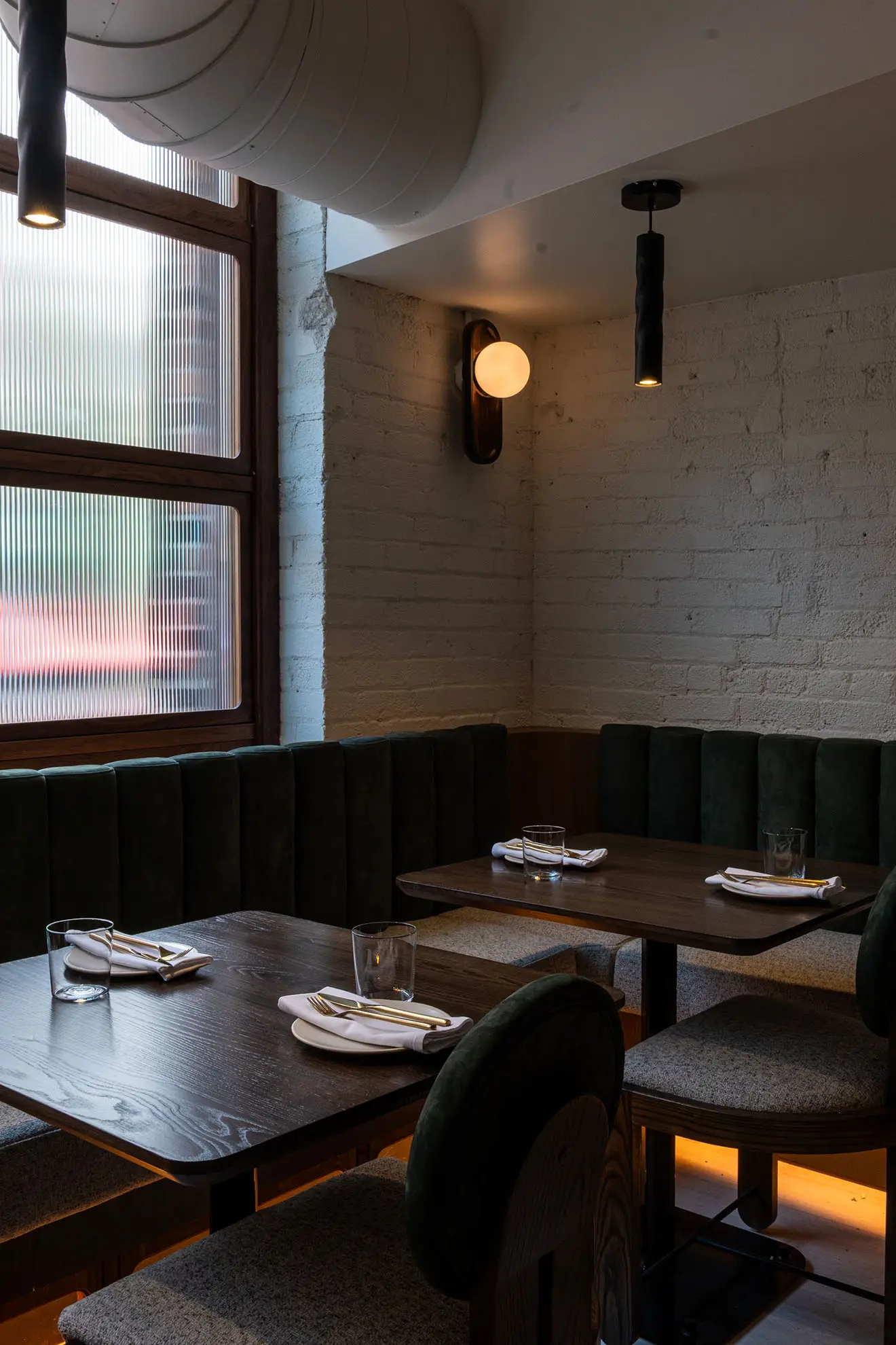 Cozy corner in a restaurant with two dark wood tables set with plates, napkins, utensils, and glasses, surrounded by upholstered seating and soft lighting.