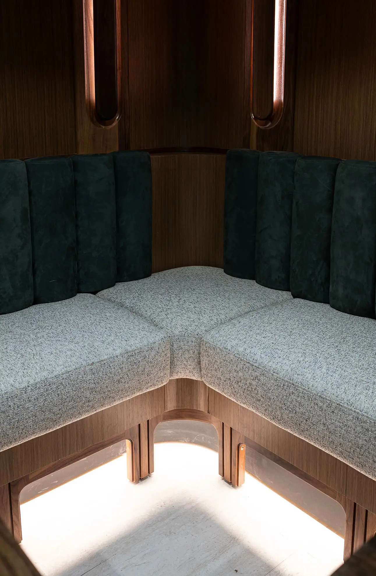 Corner seating area with dark green cushioned backs and light gray upholstered seats in a wooden-paneled room.