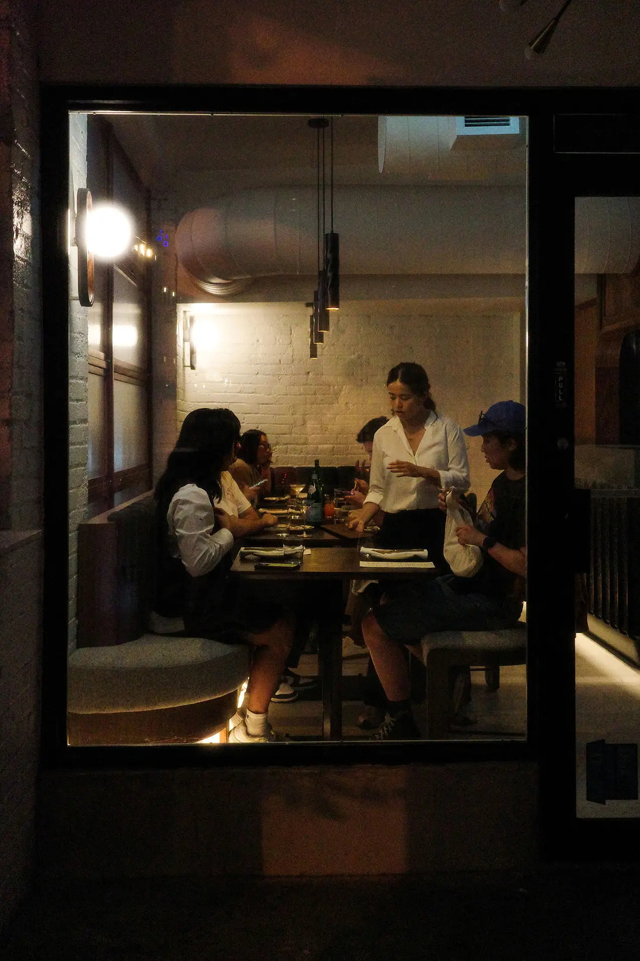 People seated around a restaurant table inside, with a server attending to them in warm, dim lighting.