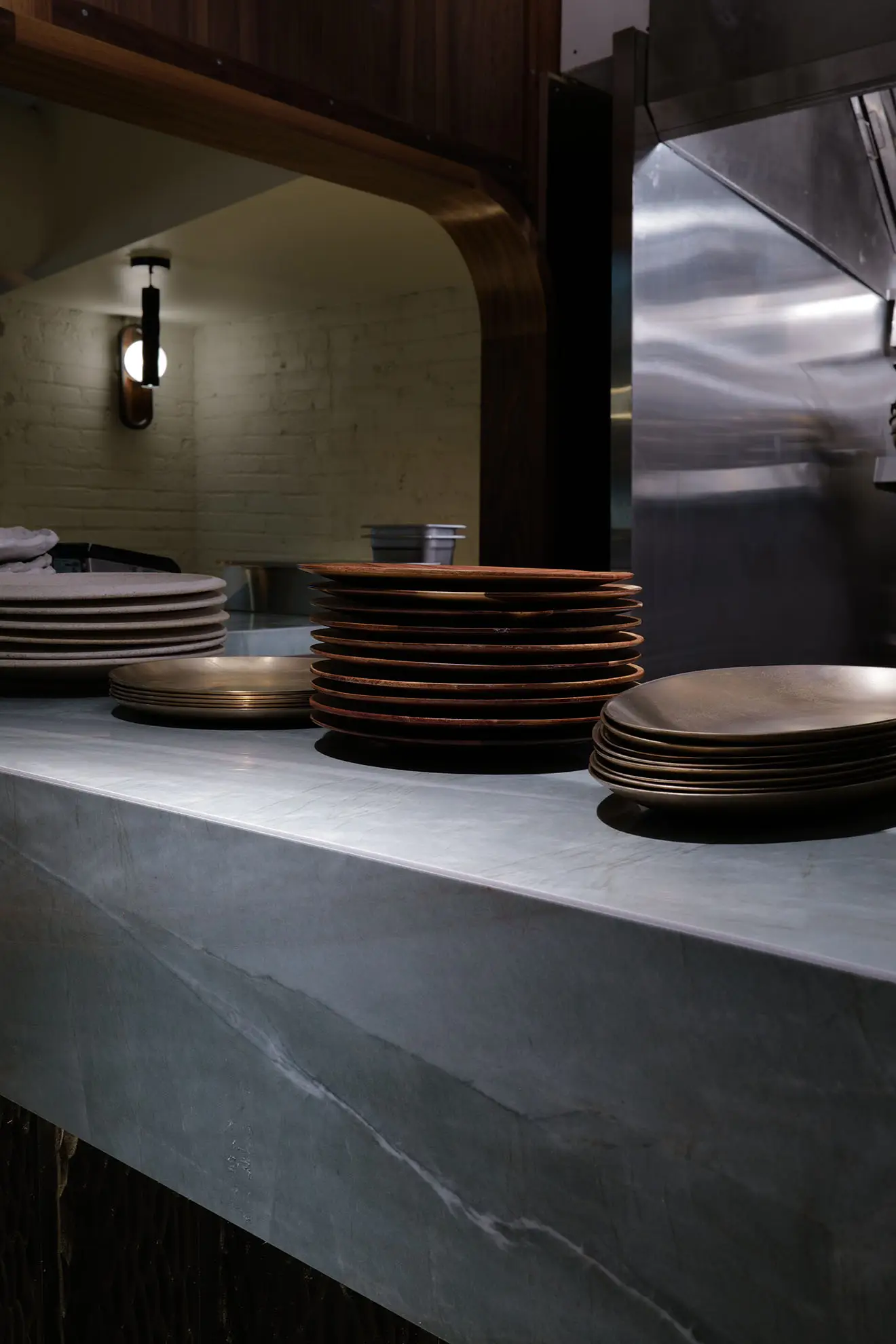 Stacks of clean plates arranged on a marble countertop in a dimly lit kitchen area.
