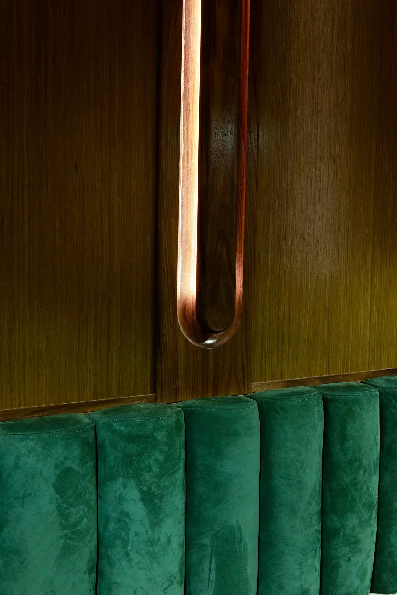 Dark green velvet cushioned seating against a wood-paneled wall with a vertically elongated oval light fixture.
