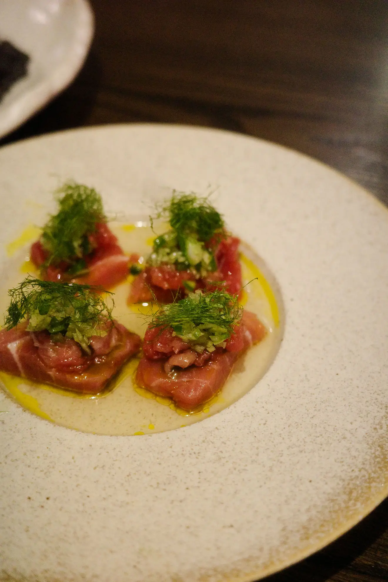 Plate with four pieces of raw fish topped with green herbs and drizzled with oil.
