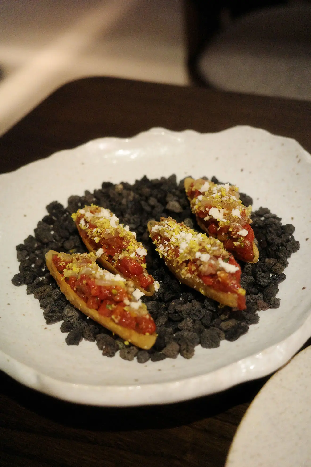 Four small appetizer bites, served on black pebbles in a white ceramic bowl.