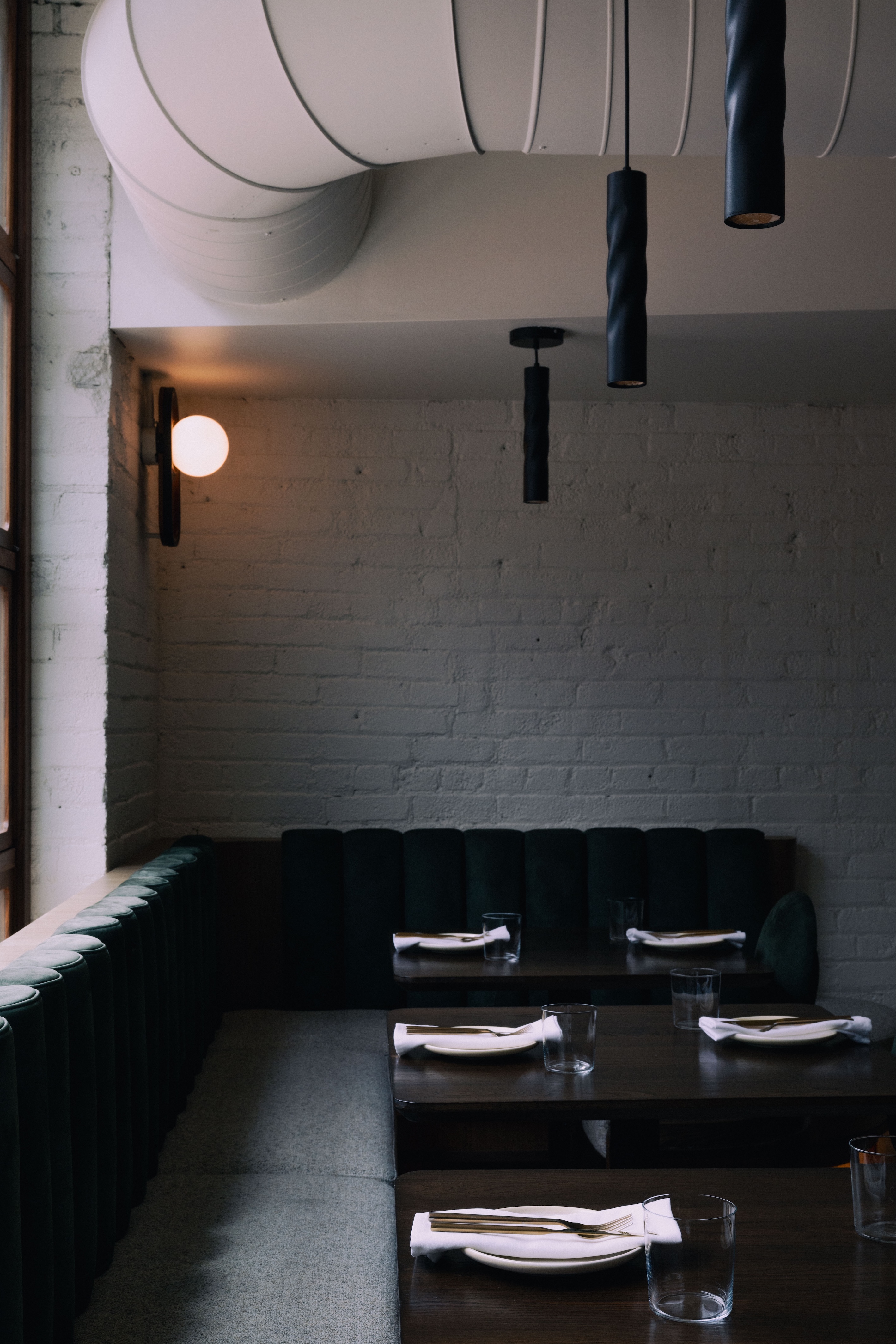 Cozy corner in a restaurant with two dark wood tables set with plates, napkins, utensils, and glasses, surrounded by upholstered seating and soft lighting.