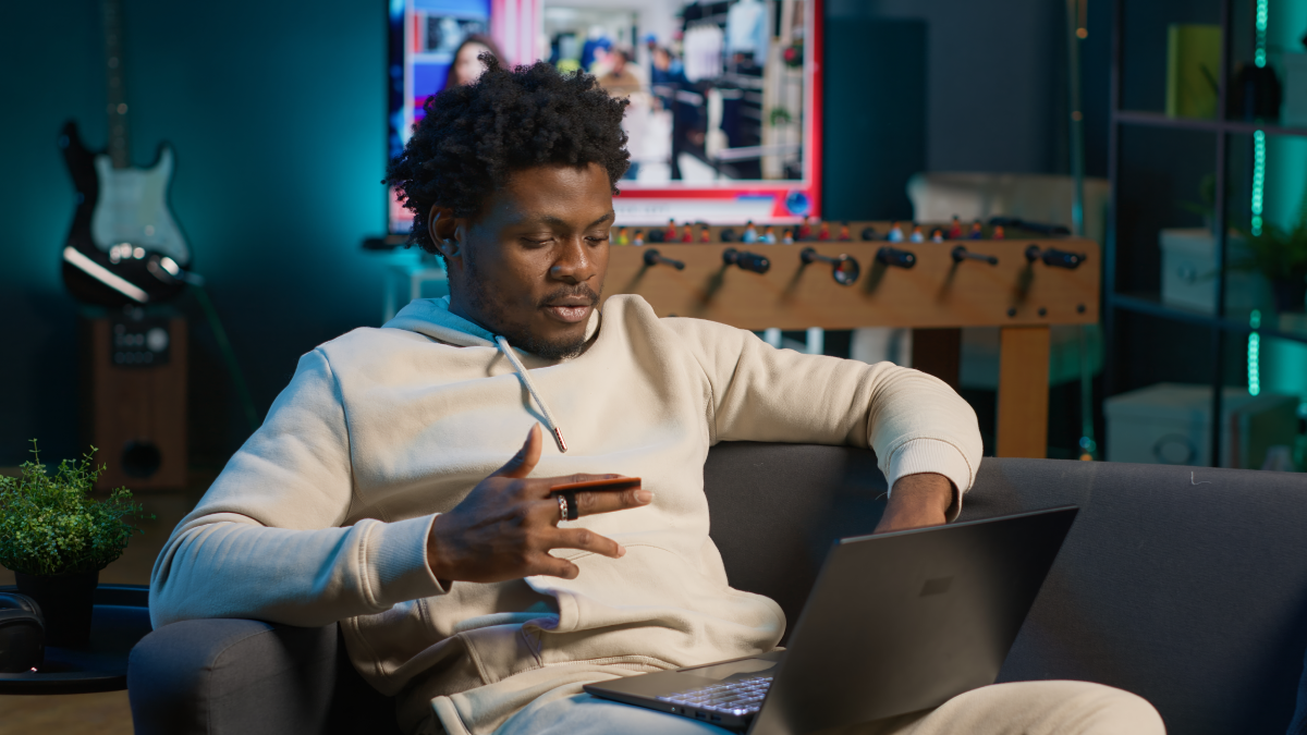 A man sitting in his room and looking at the laptop while holding a credit card in his hand
