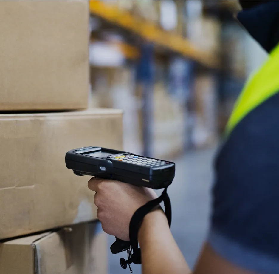 A person holding a barcode scanner in front of a stack of boxes.