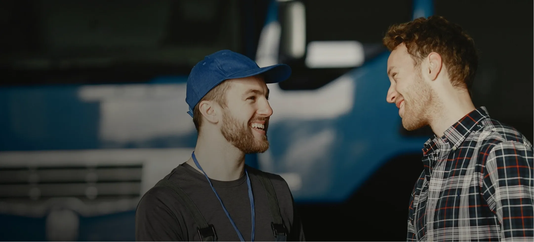 Two men talking to each other in front of a blue truck.