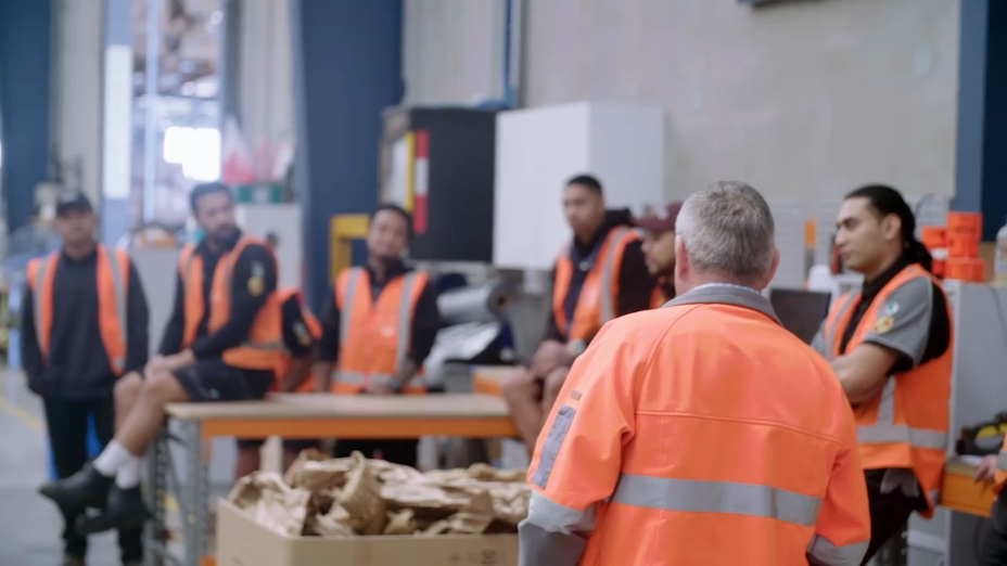 A man in an orange vest stands in front of a group of other men.