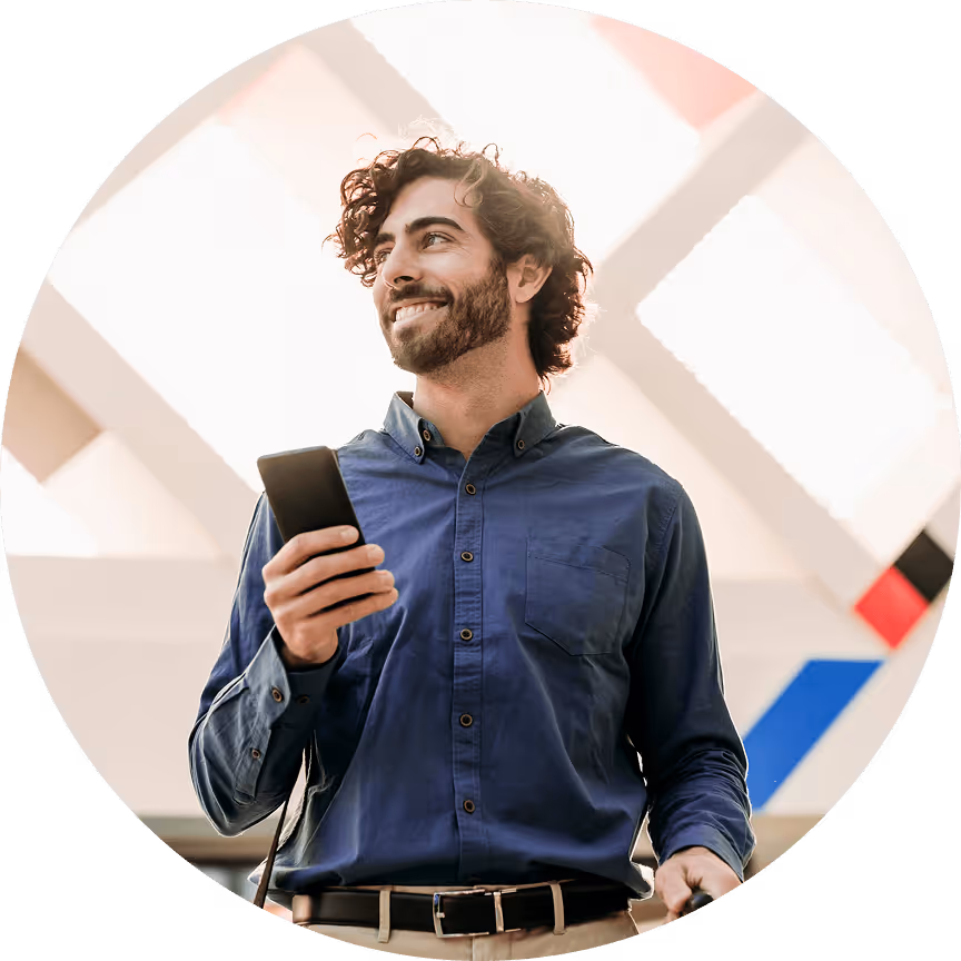 Smiling man with curly hair dressed in a button down shirt and holding a cell phone.