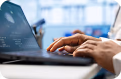 Person typing on a laptop keyboard with a blurred background of a bright office or workspace.