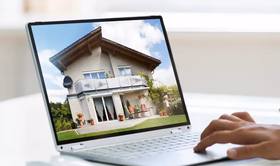 Person using a laptop displaying an image of a modern two-story house with a balcony and garden.