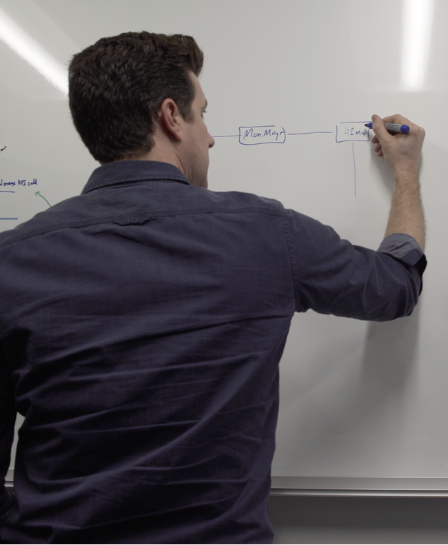 Man writing a flowchart diagram on a whiteboard with a blue marker.