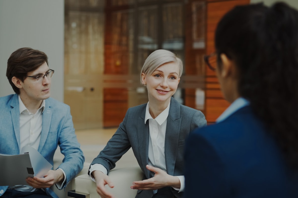 Three business professionals in a serious meeting room discussion, with two founders presenting across a table to a third party