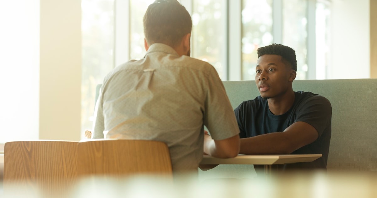 Two colleagues in a focused one-on-one conversation at a desk, modeling the candid feedback loops founders need to build.