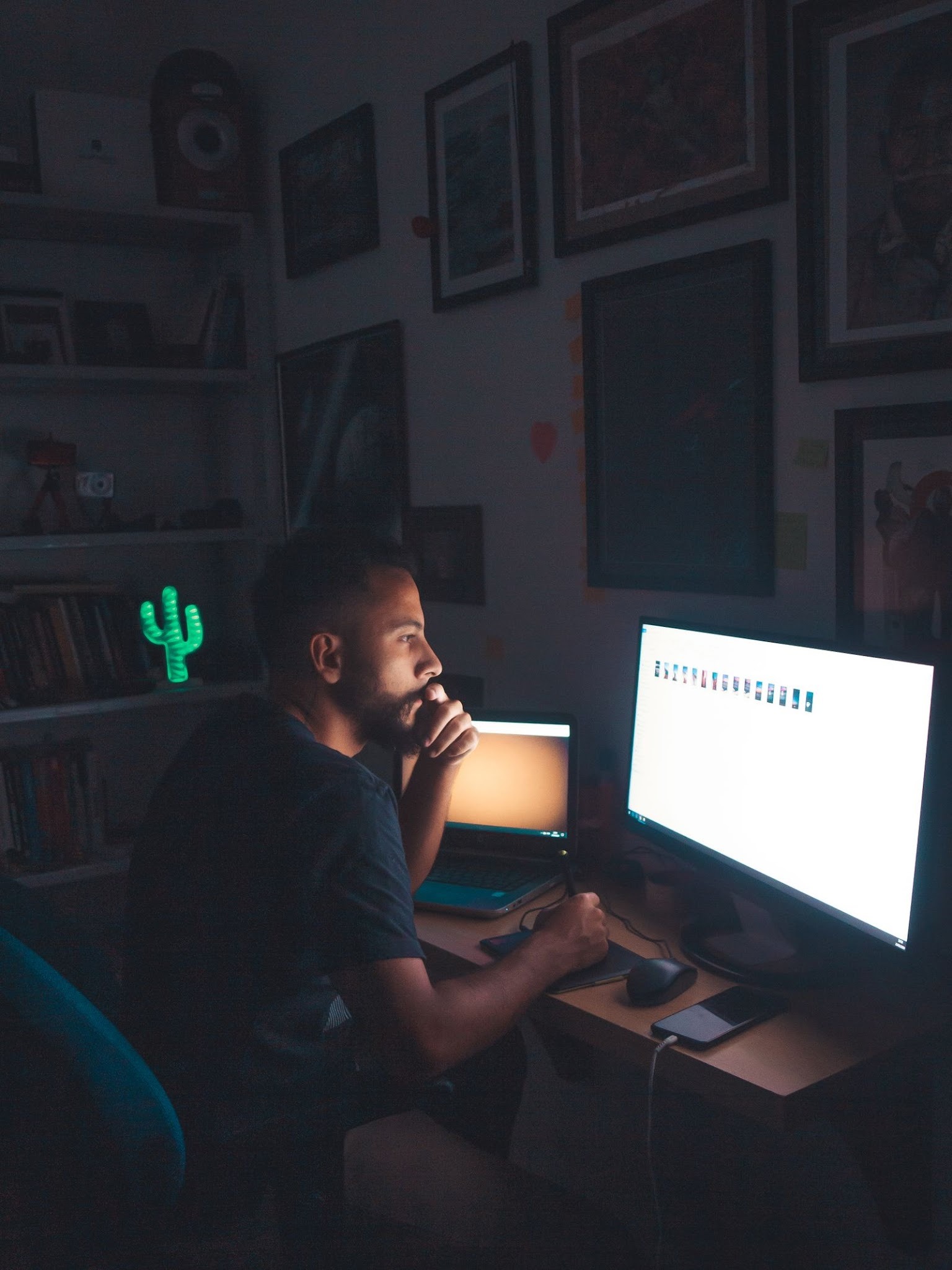 A lone man sits in a darkened room, his face lit only by the glow of a computer screen at night.
