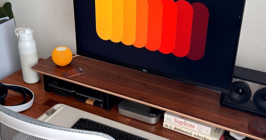 A clean, uncluttered walnut desk with a monitor riser, keyboard, and water bottle, evoking a calm, low-distraction founder workspace.