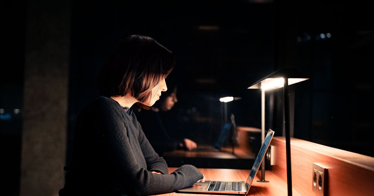 A person working late at a laptop in a dimly lit room, composing a long message.