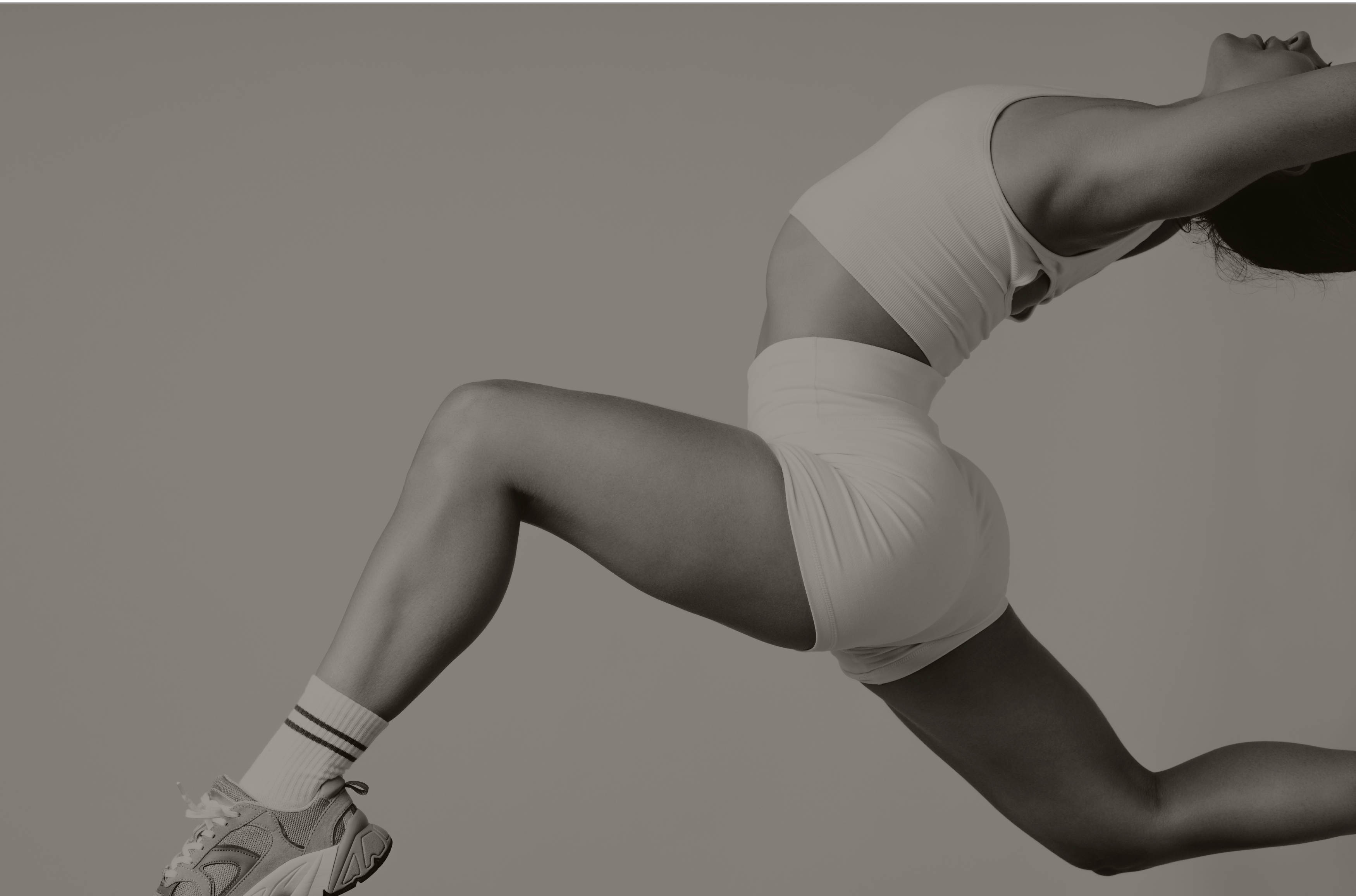 Woman in white sportswear and sneakers performing a high lunge with arms extended backward.