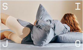 Person with long hair lying on side on a bed hugging a pillow, wearing a striped shirt and white knee-high socks.