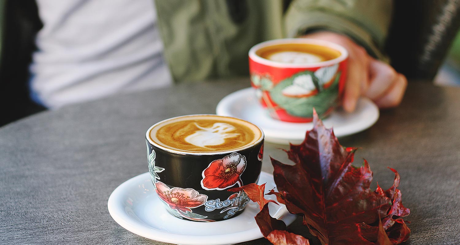 Two decorative cups of coffee on a table with a person sitting across