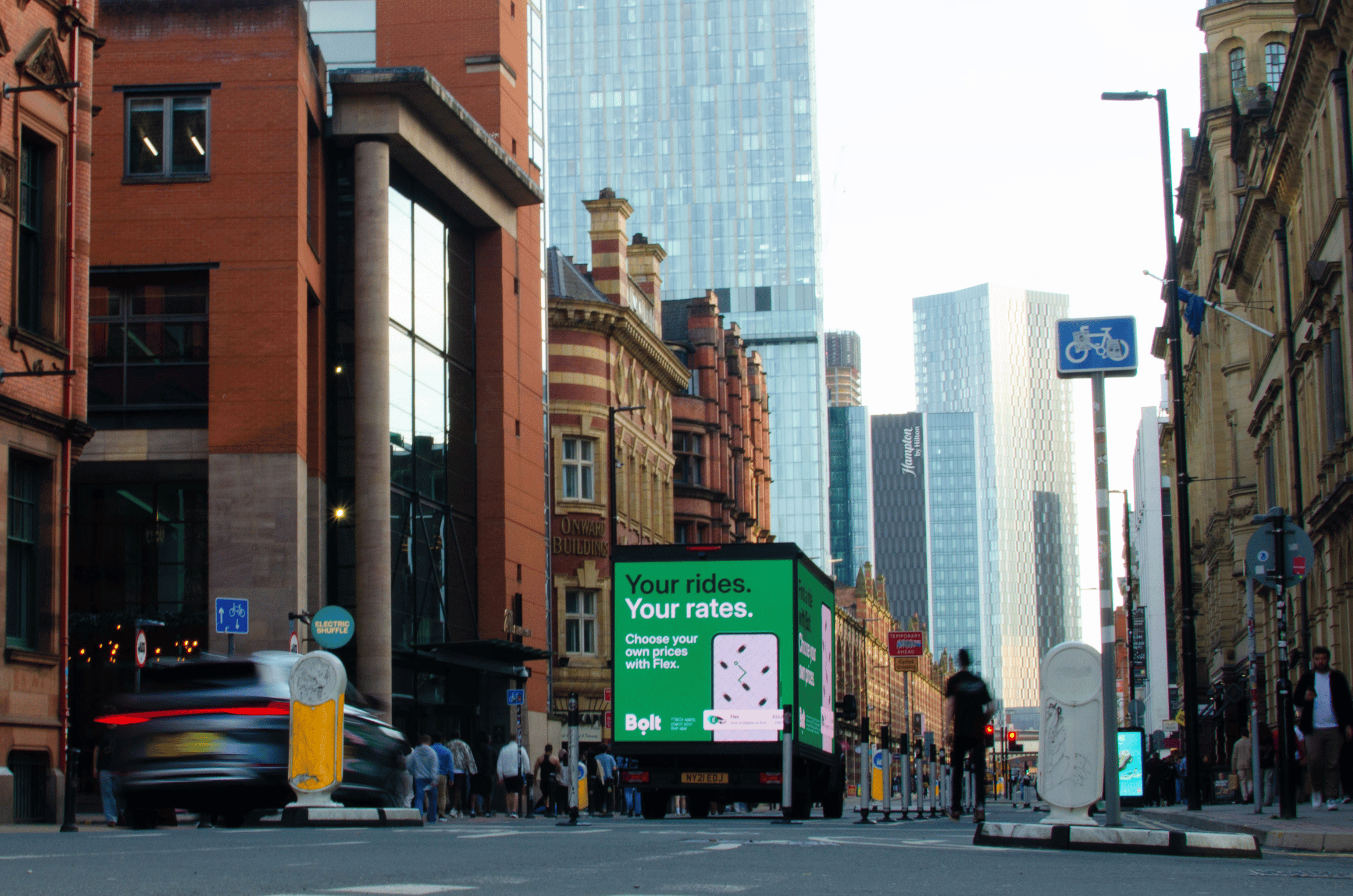 City street with a truck displaying an Antigua Barbuda beach advertisement and modern glass buildings in the background.