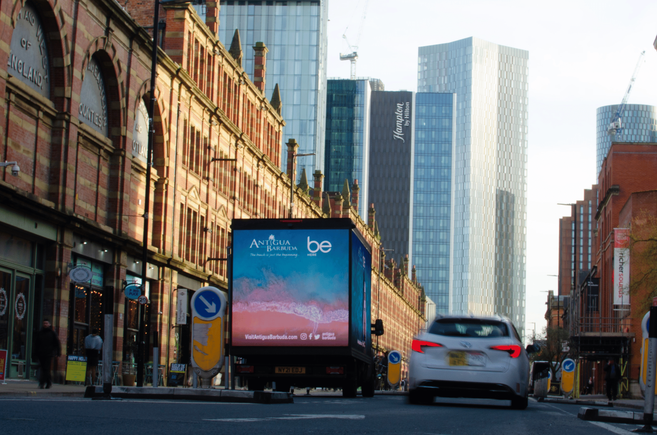 Urban street scene with historic brick buildings on the left and modern skyscrapers in the background, featuring a truck with a green Bolt advertisement on rides and rates.