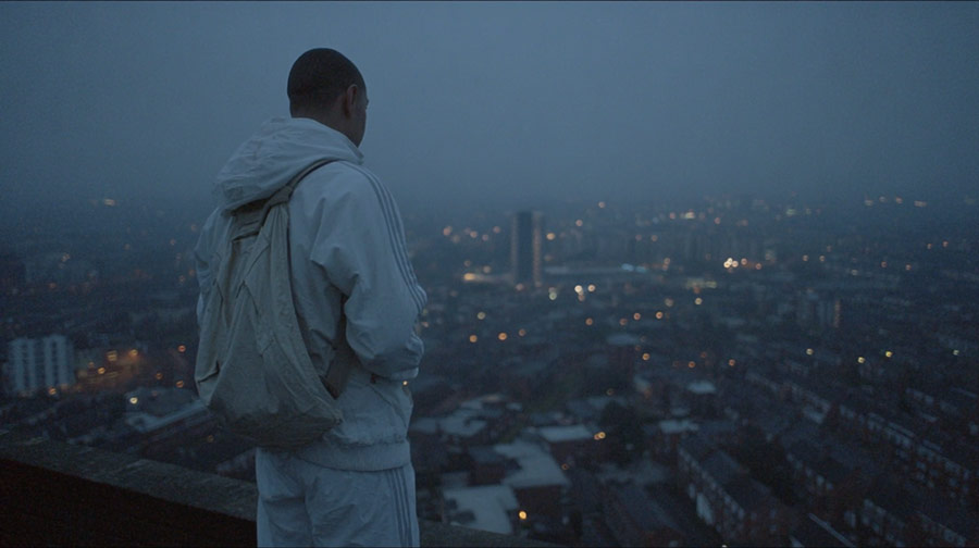 Person wearing a white jacket and backpack looking over a cityscape at dusk with scattered lights.