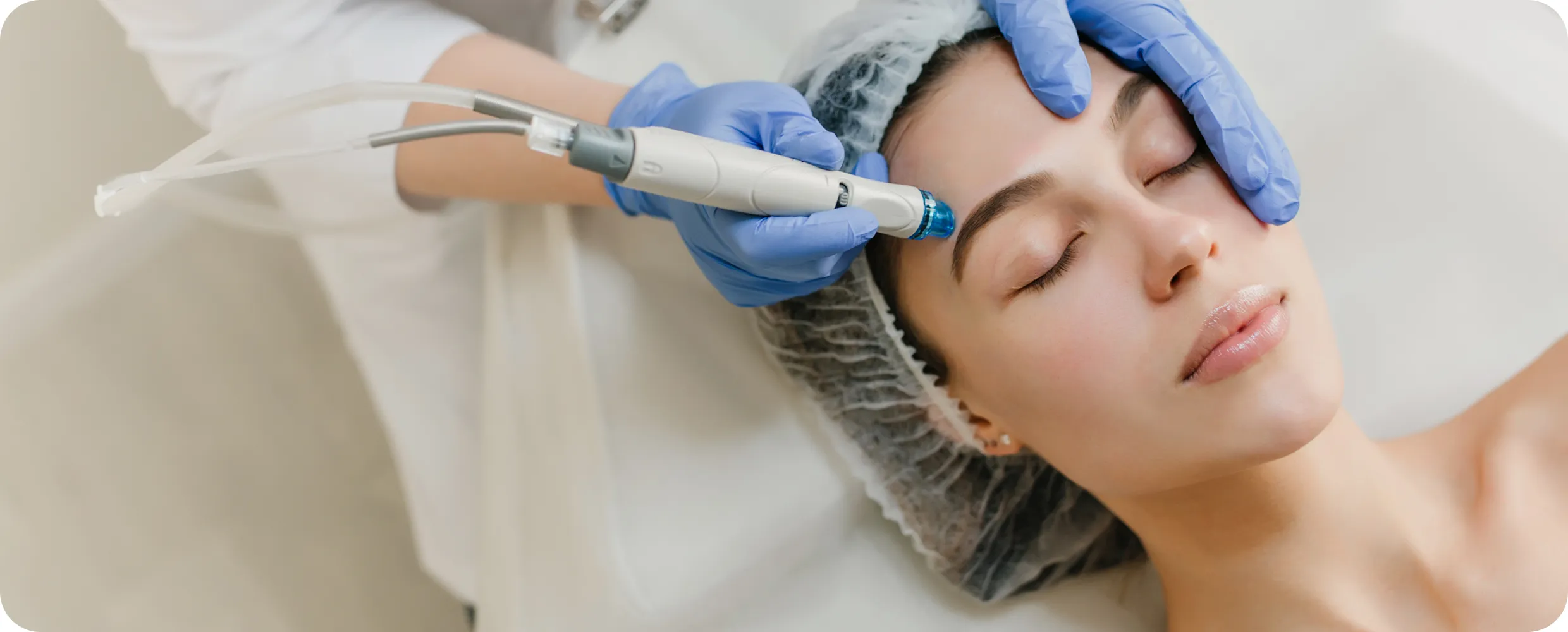 Woman receiving a facial treatment with a handheld device by a professional wearing blue gloves and a hair cap.