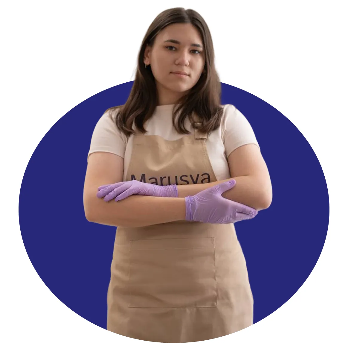 Woman with dark hair wearing a beige apron and a light pink shirt, standing with arms crossed.