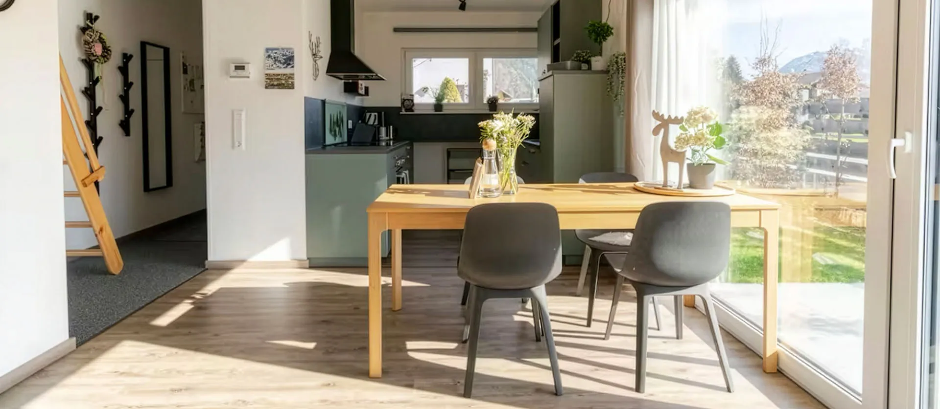 Heller Essbereich mit Holztisch, vier grauen Stühlen, Blumenvase und Schiebetür mit Blick in einen sonnigen Garten.