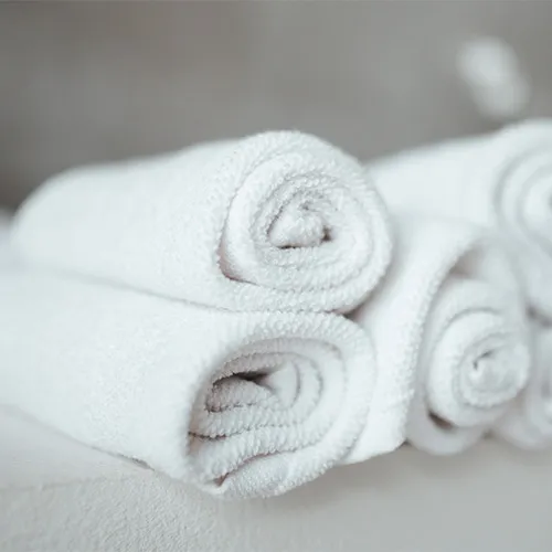 Drei weiße Handtücher ordentlich gerollt und auf einer hellen Fläche gestapelt.