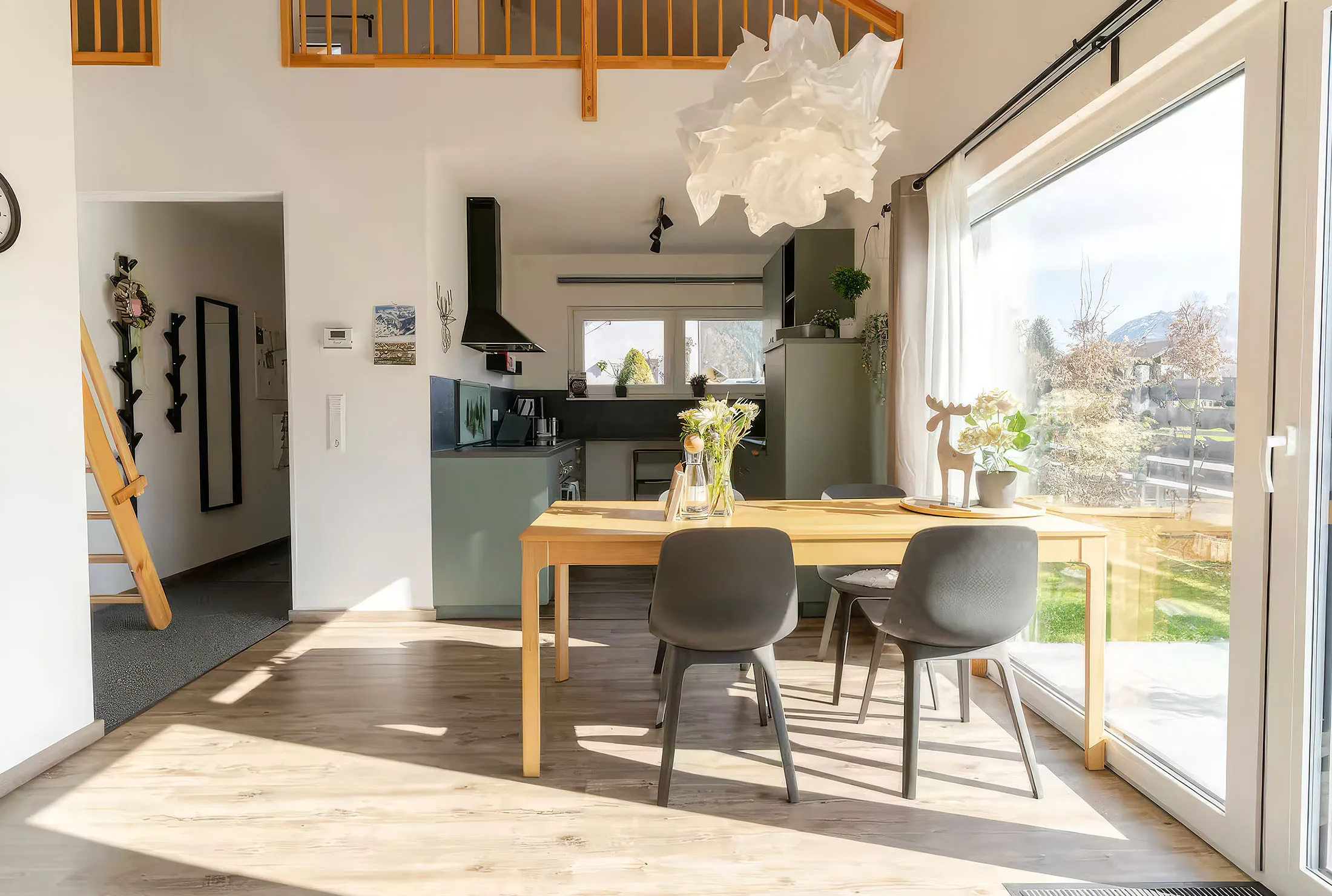 Heller Essbereich mit Holztisch, vier grauen Stühlen, dekorativen Blumen neben großem Fenster mit Blick in den Garten.