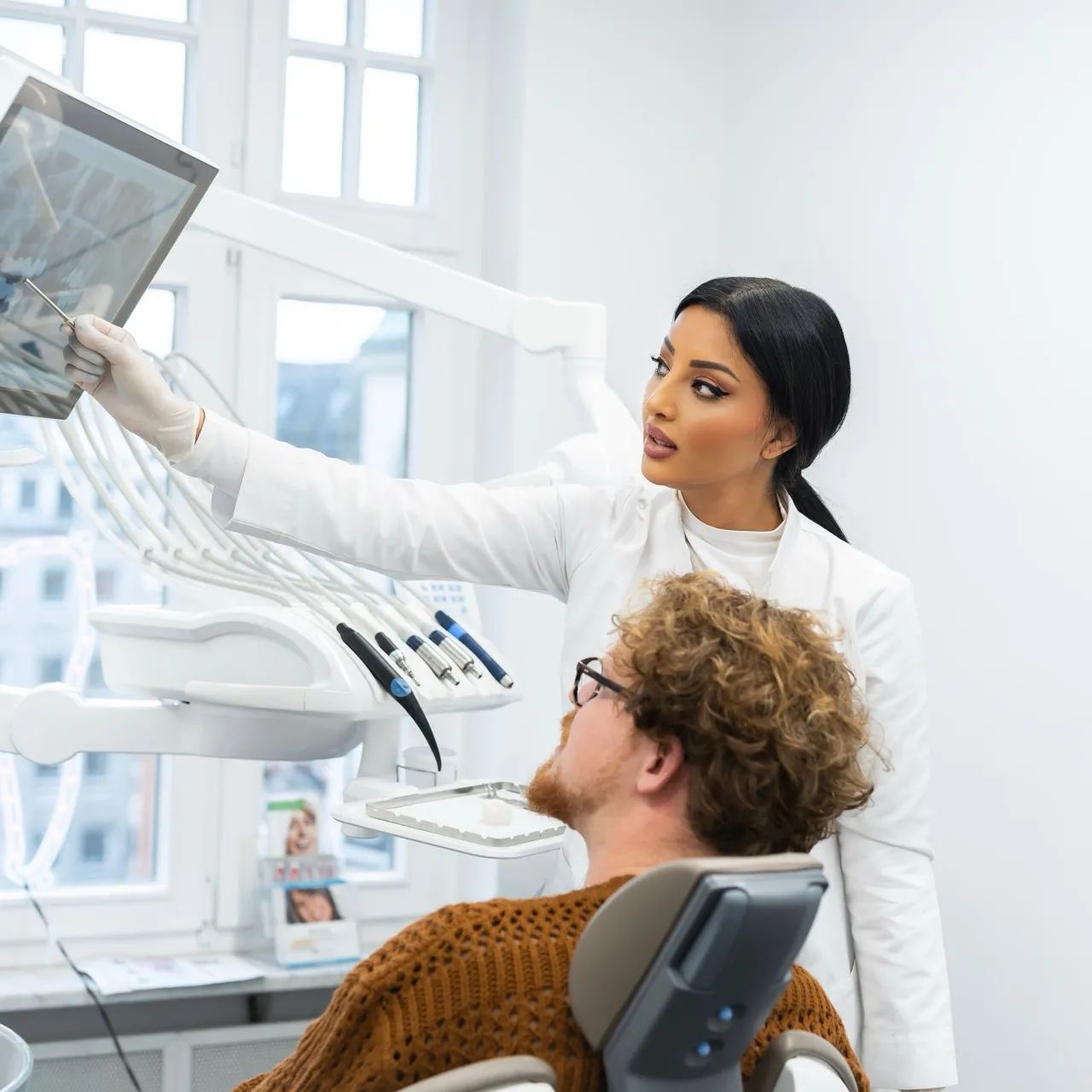 Zahnärztin zeigt einem männlichen Patienten mit Brille ein Zahn-Röntgenbild in einer modernen Zahnarztpraxis.