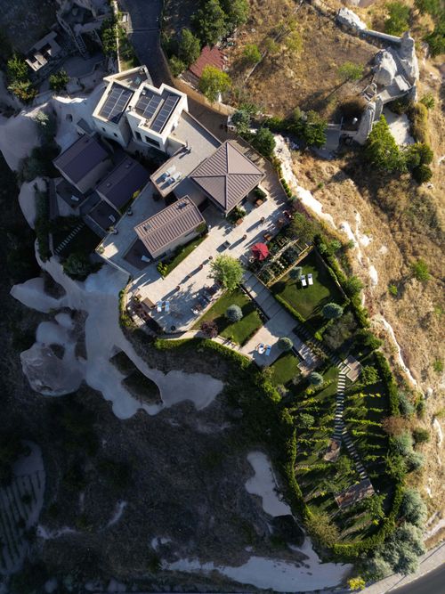 Aerial view of a modern house with solar panels, terraces, lawns, and a garden surrounded by dry grassy terrain.