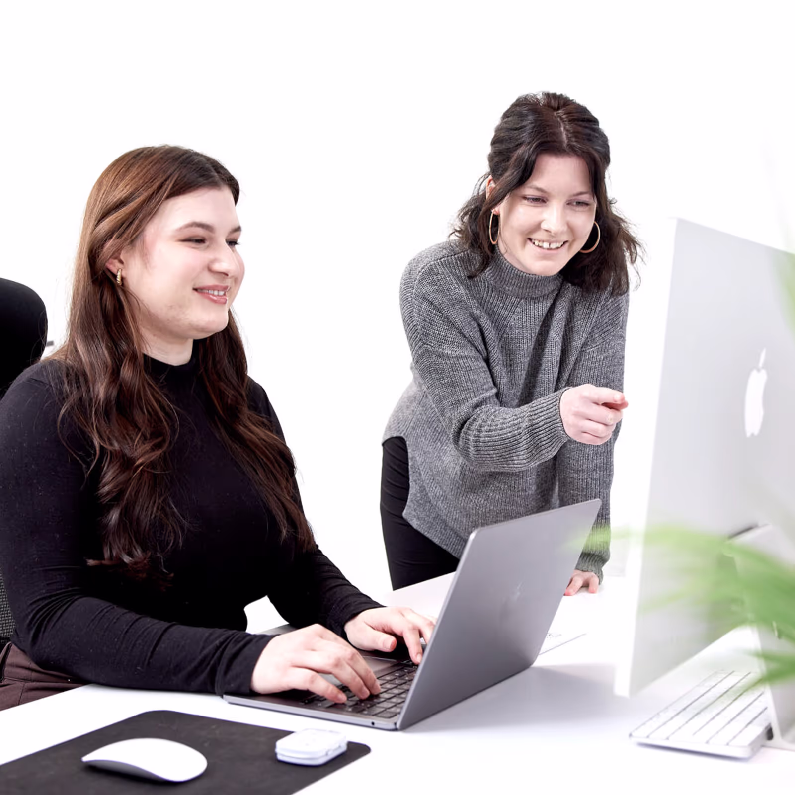 Zwei Kolleginnen arbeiten gemeinsam an einem Projekt am Computer in einem modernen, hellen Büro.