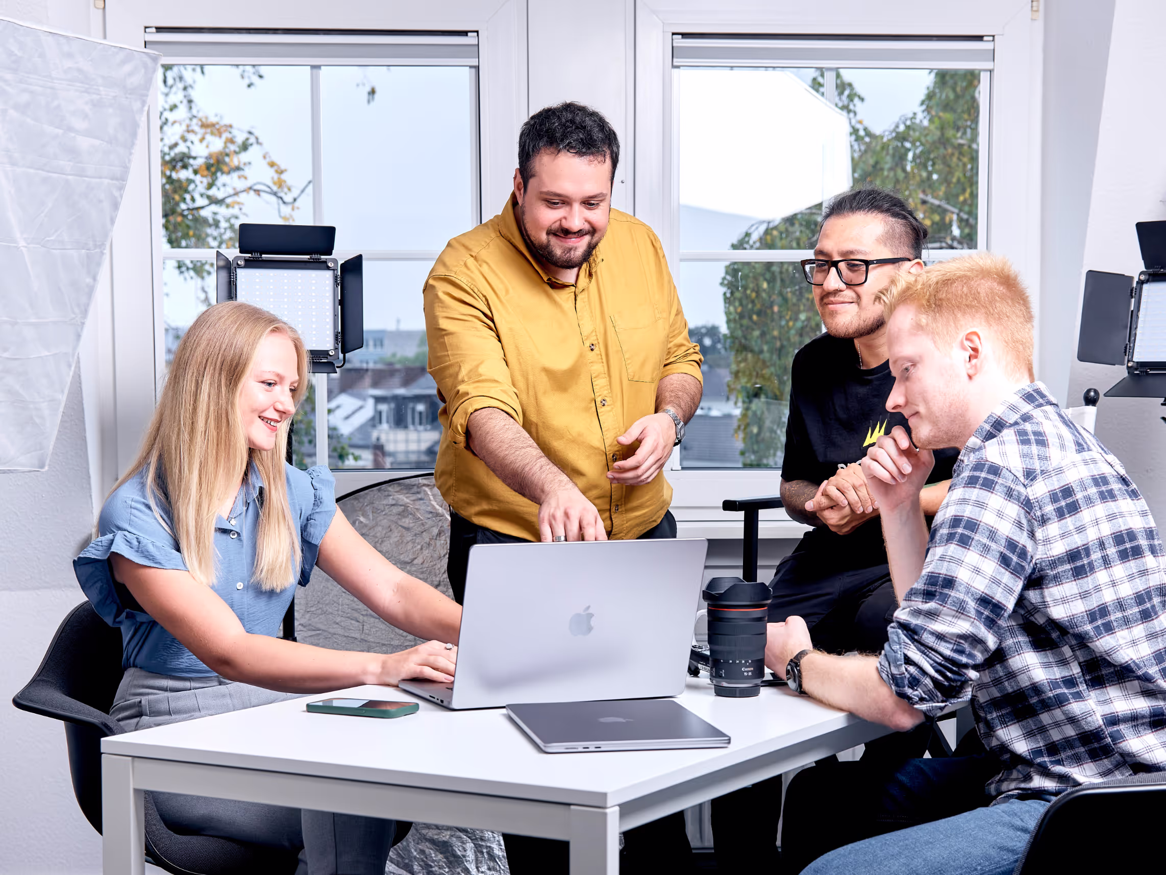 Vier Teammitglieder von PGdigital arbeiten gemeinsam an einem Laptop in einem hellen, modern ausgestatteten Büro mit Fotoequipment im Hintergrund.