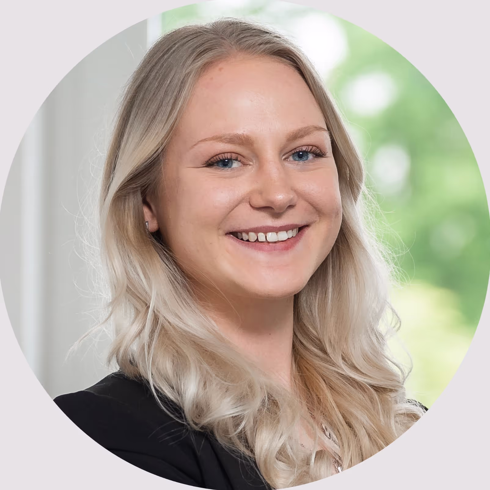 Porträt einer lächelnden jungen Frau mit langen, blonden Haaren im Business-Outfit vor einem hellen Hintergrund.