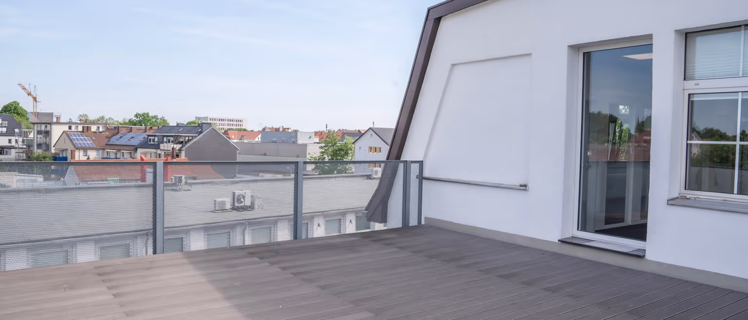 Moderne Dachterrasse eines Bürogebäudes mit Glasgeländer und Blick auf umliegende Wohnhäuser bei klarem Himmel.